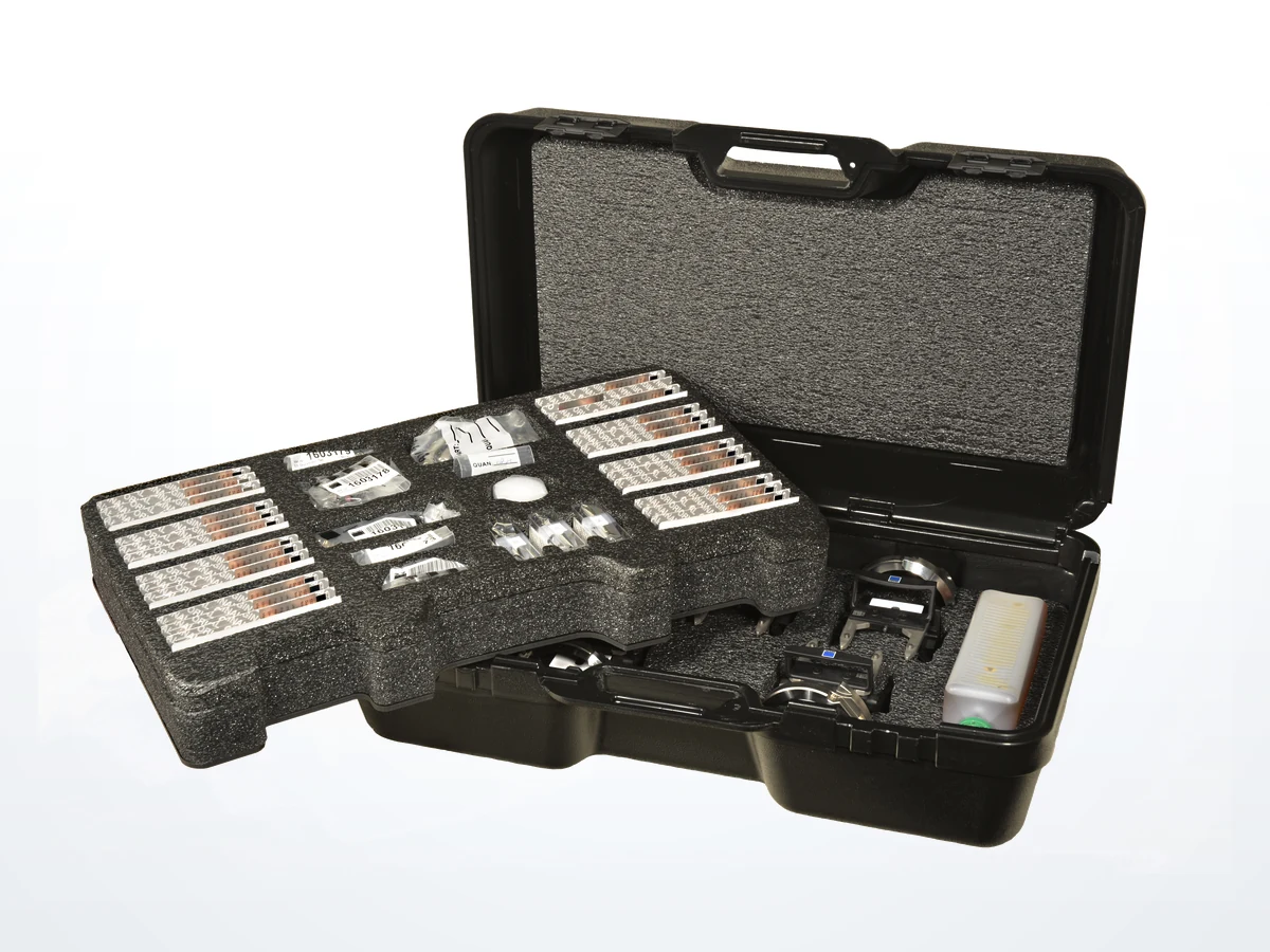 An open carrying case with a two-tier custom die-cut foam interior holding labelled components and instruments