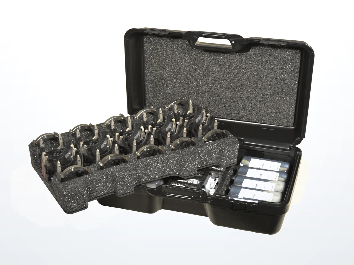 An open carrying case with a die-cut foam tray holding rows of metal tooling components and vials
